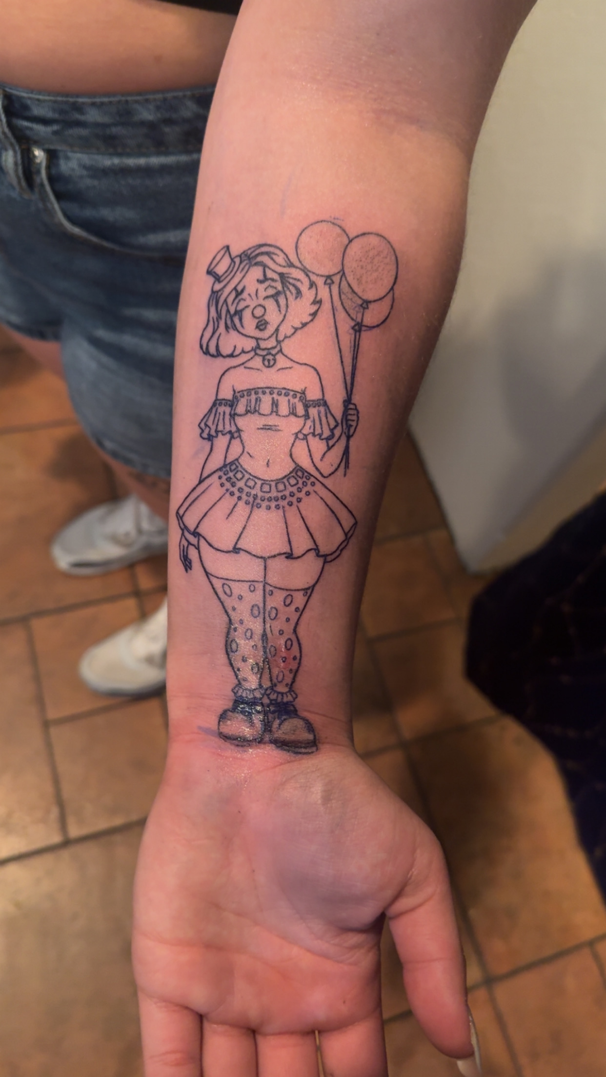 Fine line clown girl with balloons tattoo on a forearm