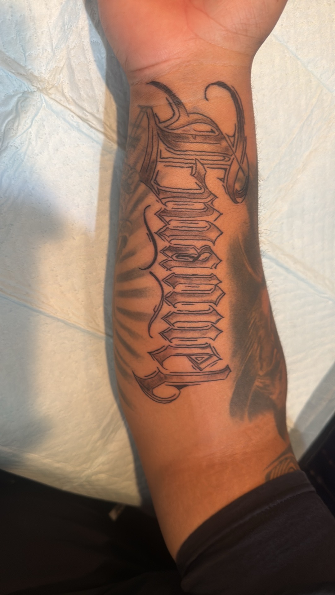 Black and grey script lettering tattoo on a forearm